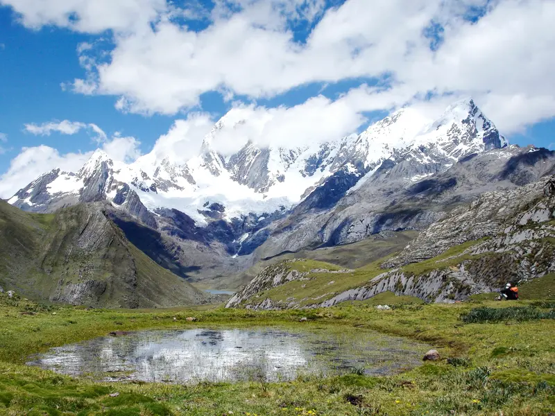 Wanderer macht eine Pause an einem klaren Bergsee mit Blick auf die schneebedeckten Gipfel der Cordillera Blanca in Peru.