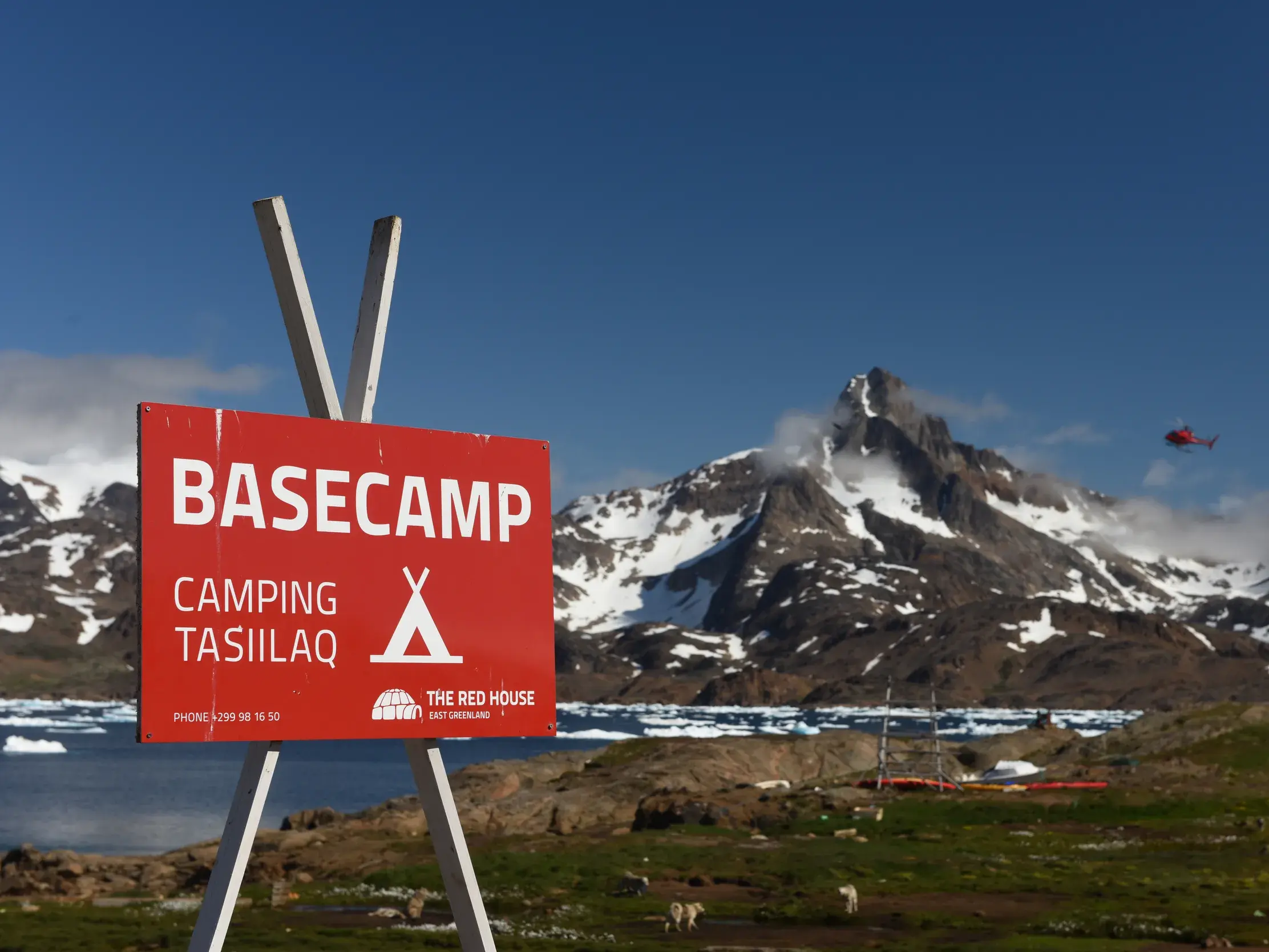 Rotes Schild des Basecamps in Tasiilaq, dem Startpunkt für Trekking-Touren in Ostgrönlands Berg- und Fjordlandschaft.