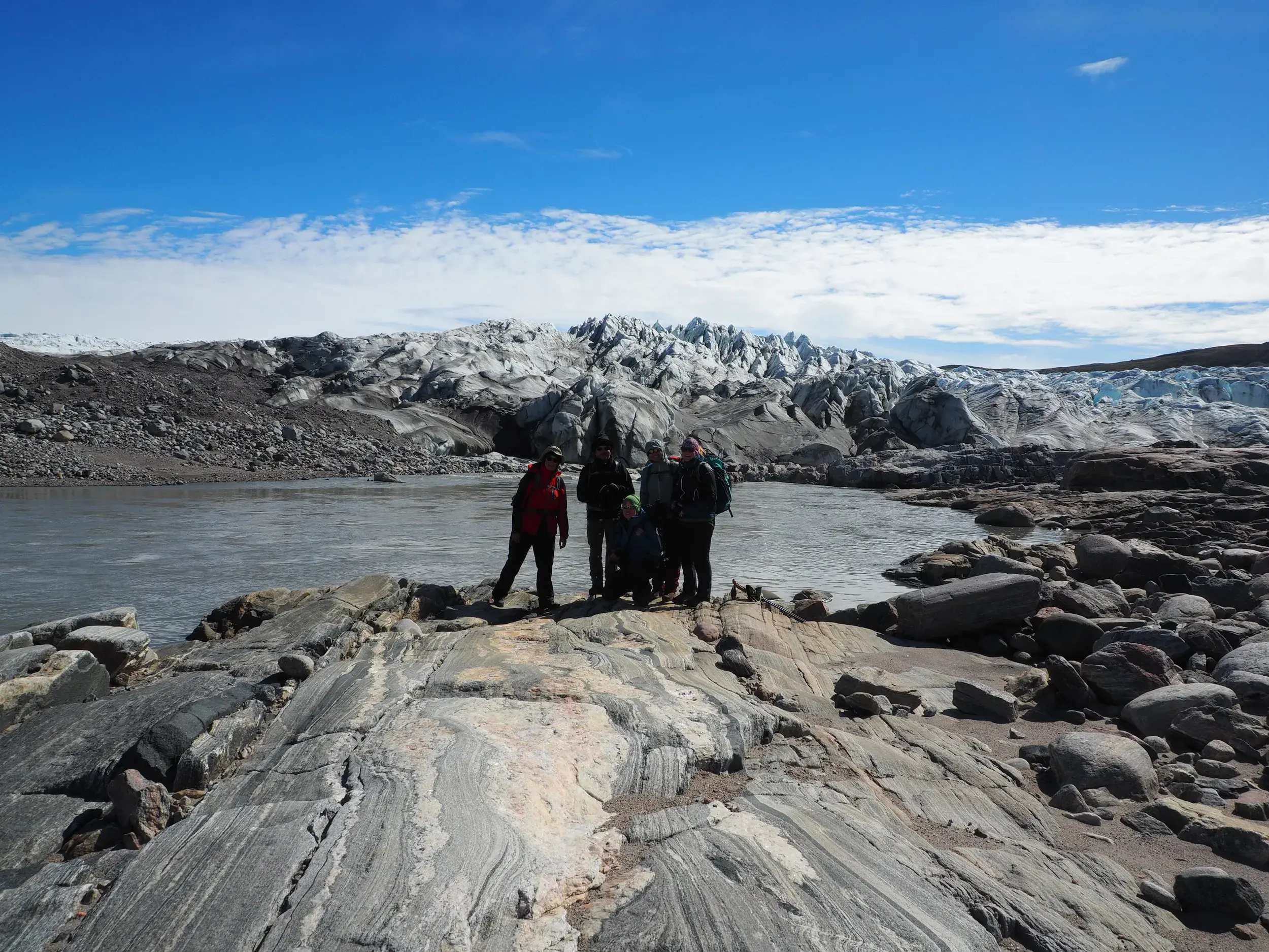 Eine Hauser-Wandergruppe posiert für ein Foto auf Felsen an der Abbruchkante des beeindruckenden Russel-Gletschers in Grönland.