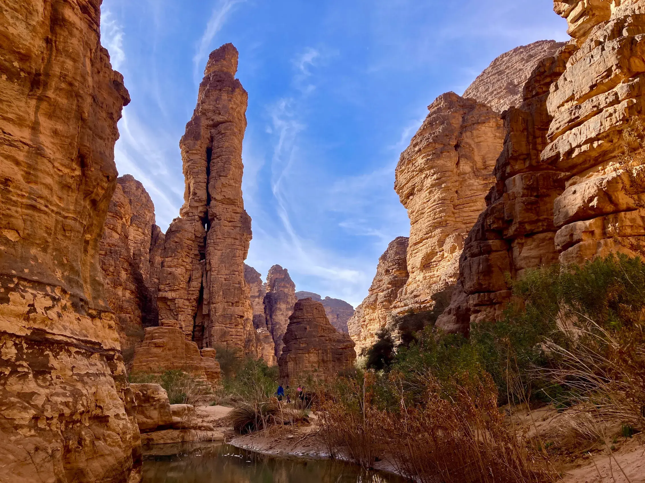 Eine Trekkinggruppe wandert durch eine Felsschlucht im Tassili n'Ajjer Nationalpark in Algerien, vorbei an einer hohen Felsnadel.