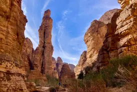 Eine Trekkinggruppe wandert durch eine Felsschlucht im Tassili n'Ajjer Nationalpark in Algerien, vorbei an einer hohen Felsnadel.