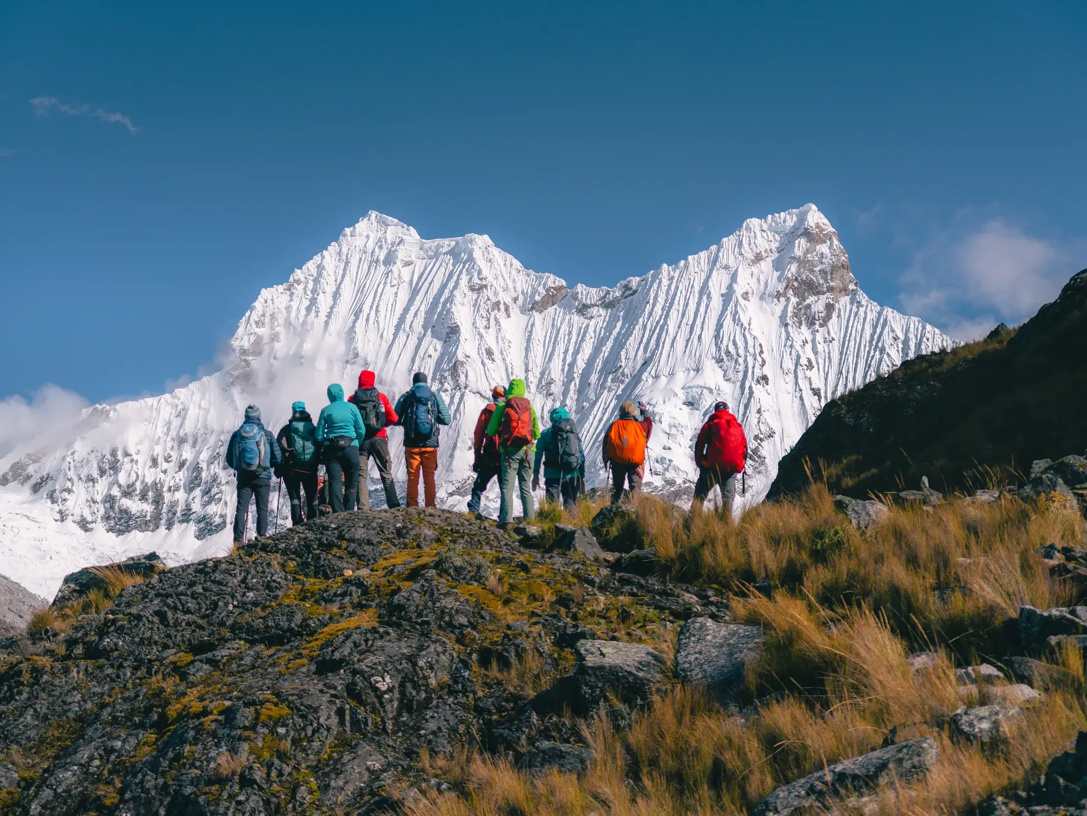 Eine Wandergruppe steht auf einem Felsen und blickt auf einen schneebedeckten Gipfel in der Cordillera Blanca in Peru.