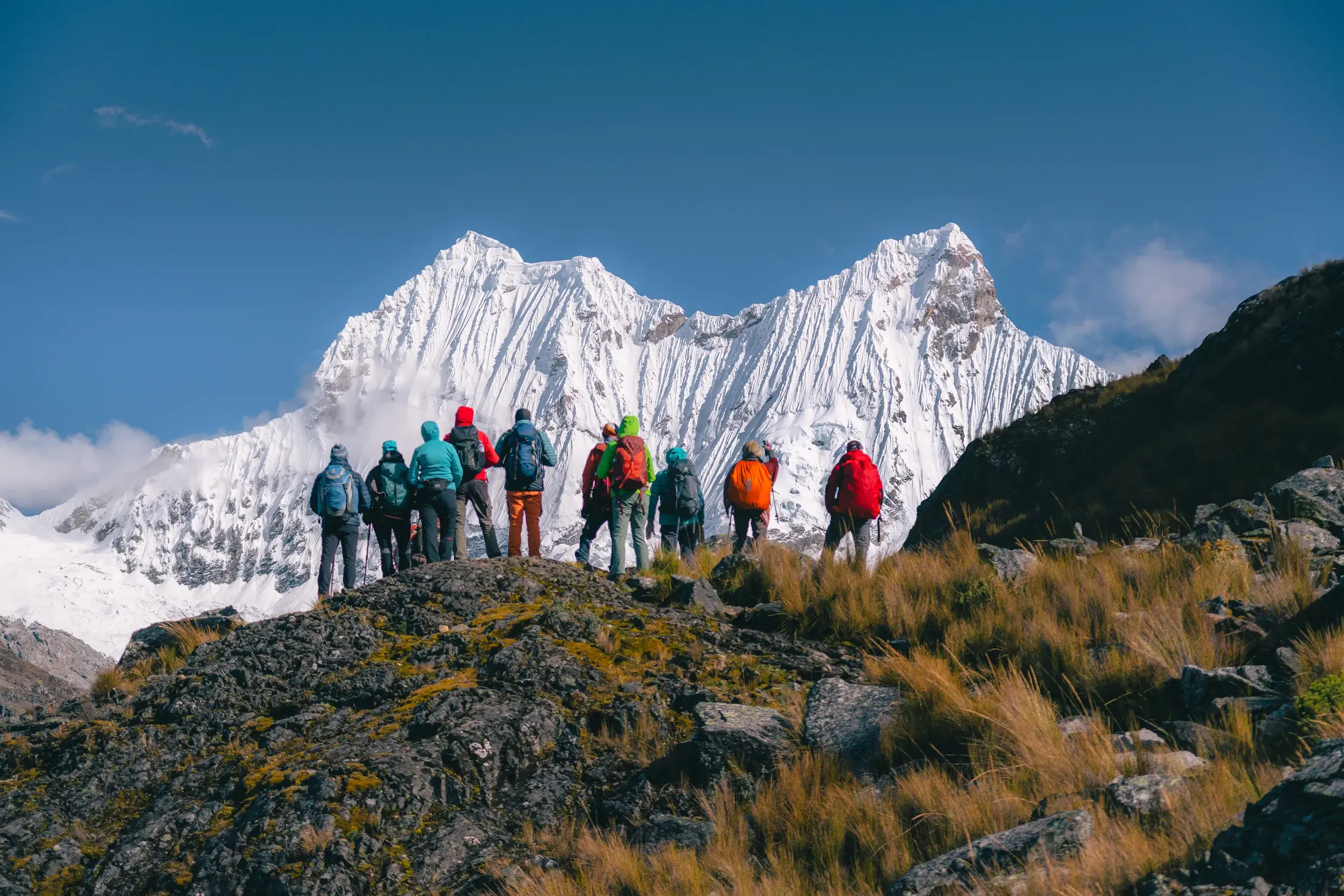 Eine Wandergruppe steht auf einem Felsen und blickt auf einen schneebedeckten Gipfel in der Cordillera Blanca in Peru.