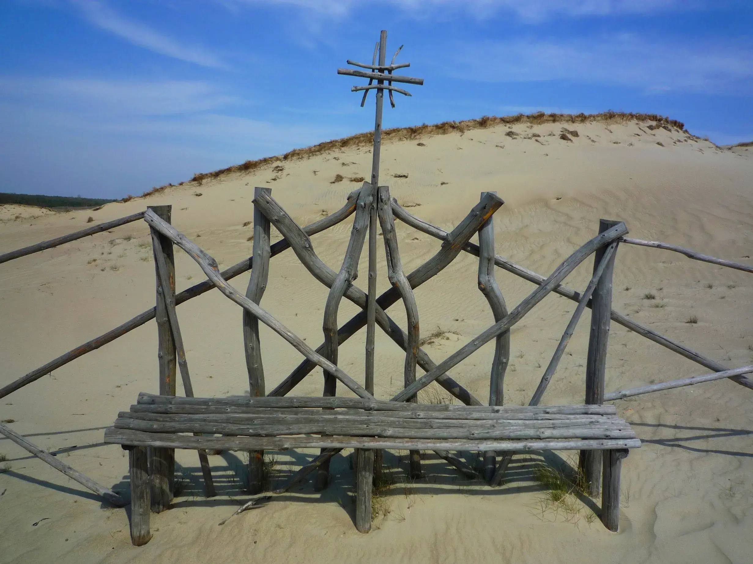 Eine kunstvolle, aus Holz gefertigte Bank in der sonnigen Dünenlandschaft auf der Kurischen Nehrung in Litauen.