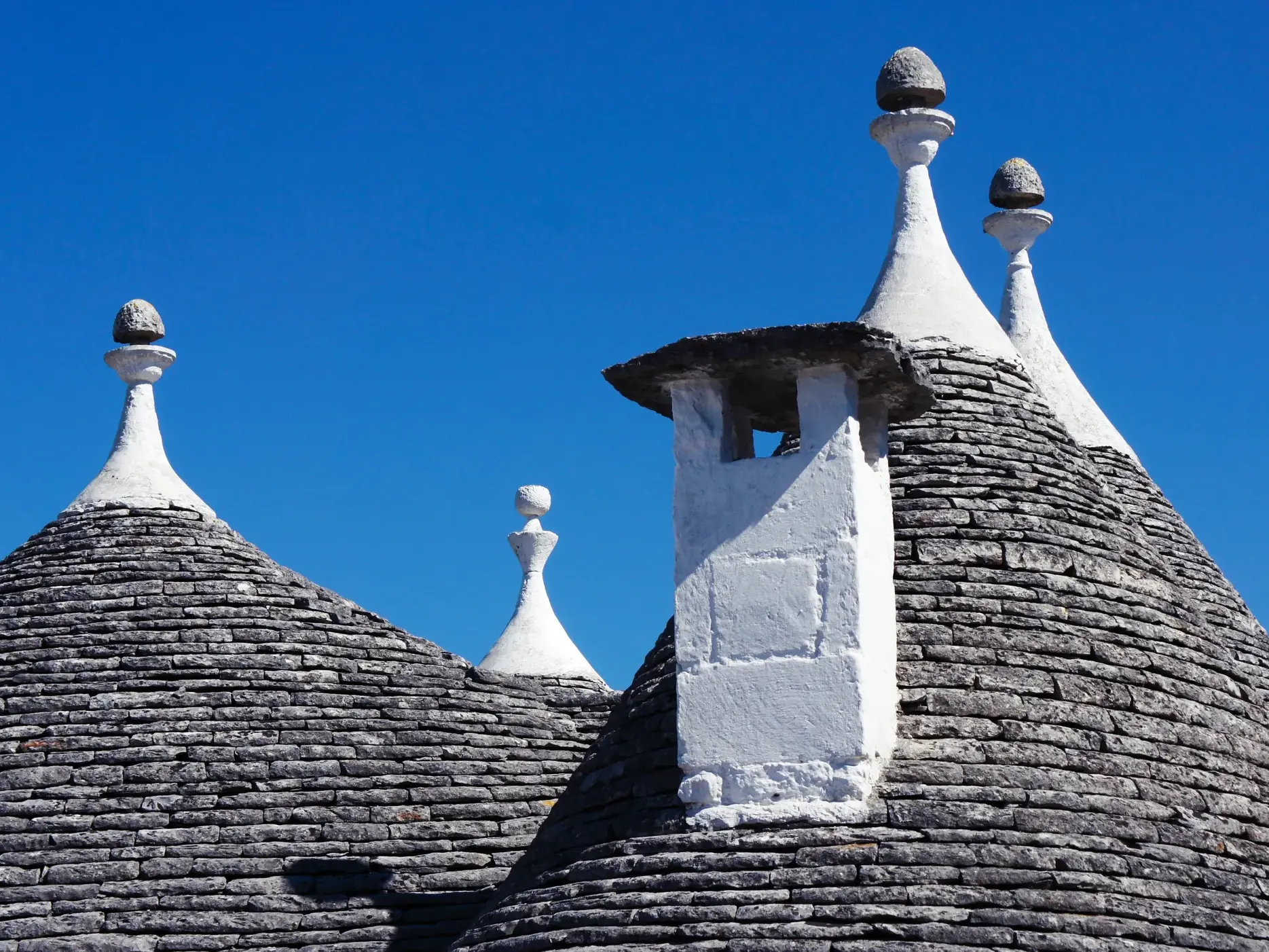 Die kegelförmigen Steindächer der Trulli, UNESCO-Weltkulturerbe in Alberobello, vor strahlend blauem Himmel in Apulien.