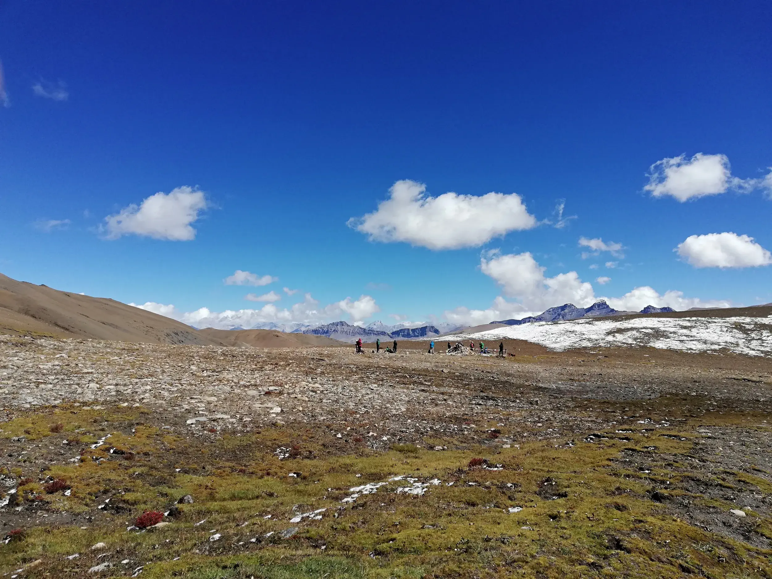 Eine Hauser-Trekkinggruppe durchquert eine karge Hochebene im Inneren Dolpo mit Blick auf die schneebedeckten Himalaya-Gipfel.