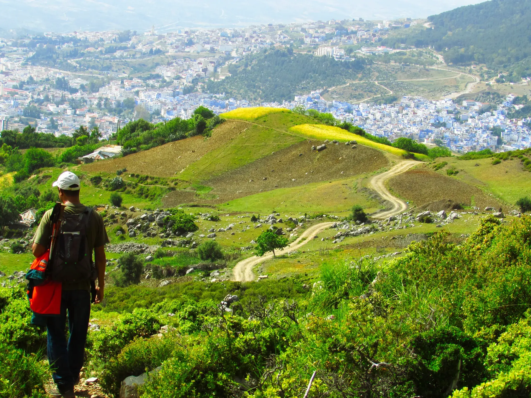 Ein Wanderer mit Rucksack auf einem Pfad im Rif-Gebirge mit Panoramablick auf die berühmte blaue Stadt Chefchaouen.