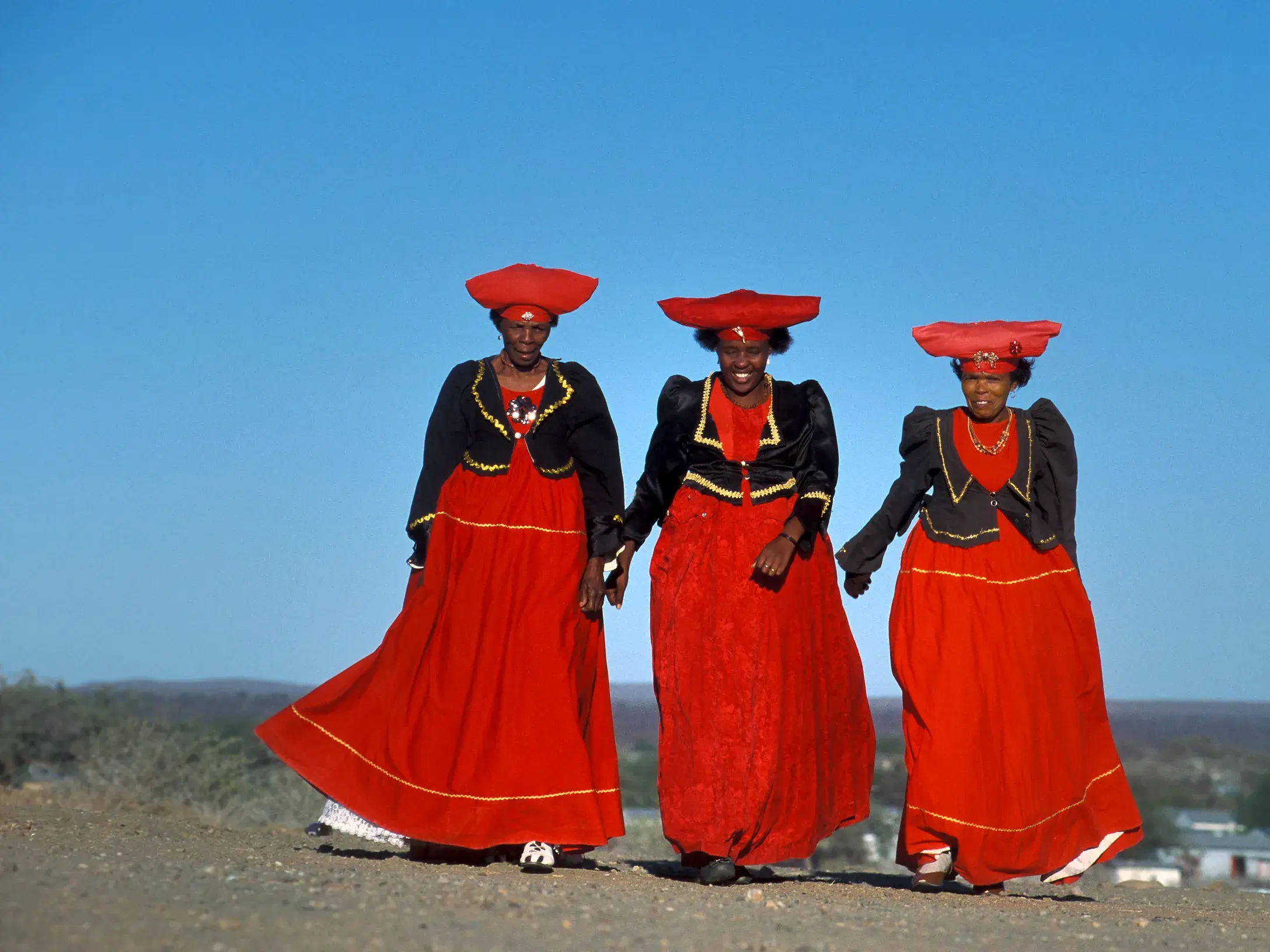 Drei Frauen vom Volksstamm der Herero in traditioneller roter Tracht mit auffälligem Kopfschmuck in Namibia.