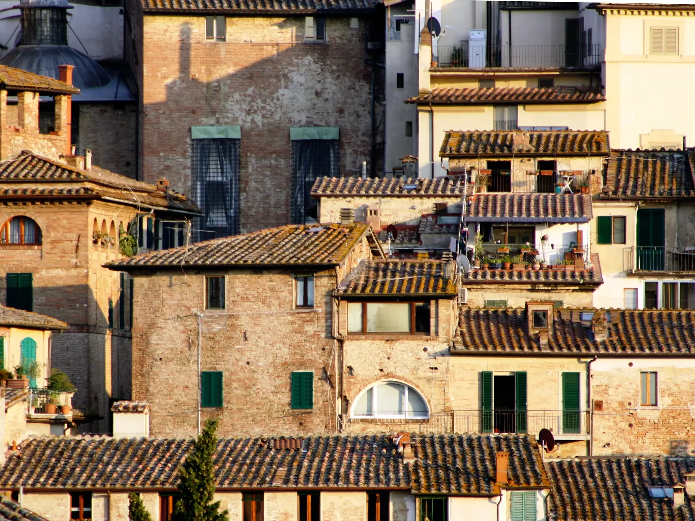 Historische Backsteingebäude und Terrakotta-Dächer in der Altstadt von Siena, Toskana, im warmen Abendlicht.