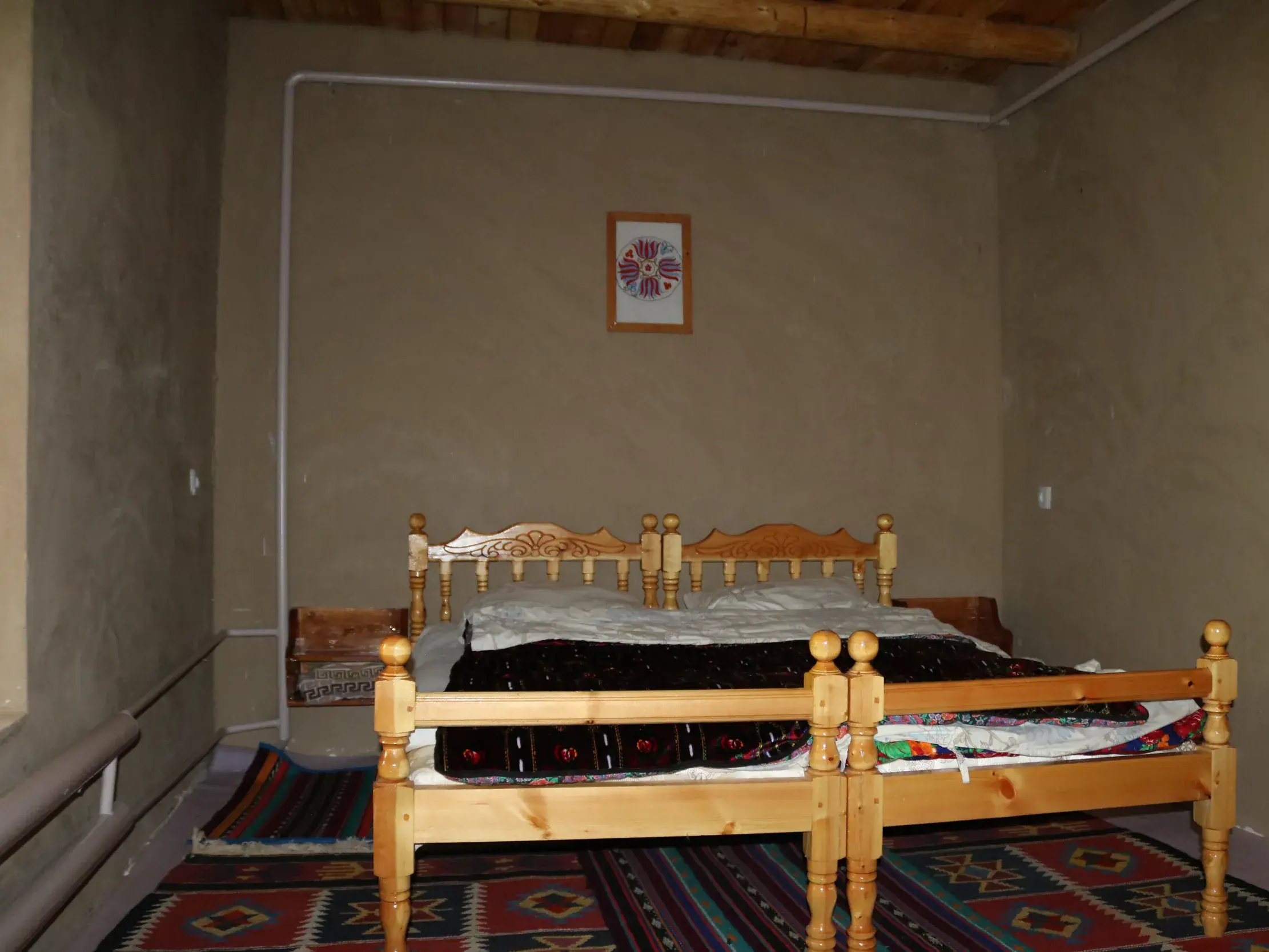 Traditionelles Gästezimmer bei einer Gastfamilie im Nuratau-Gebirge mit zwei Holzbetten und bunten Webteppichen.