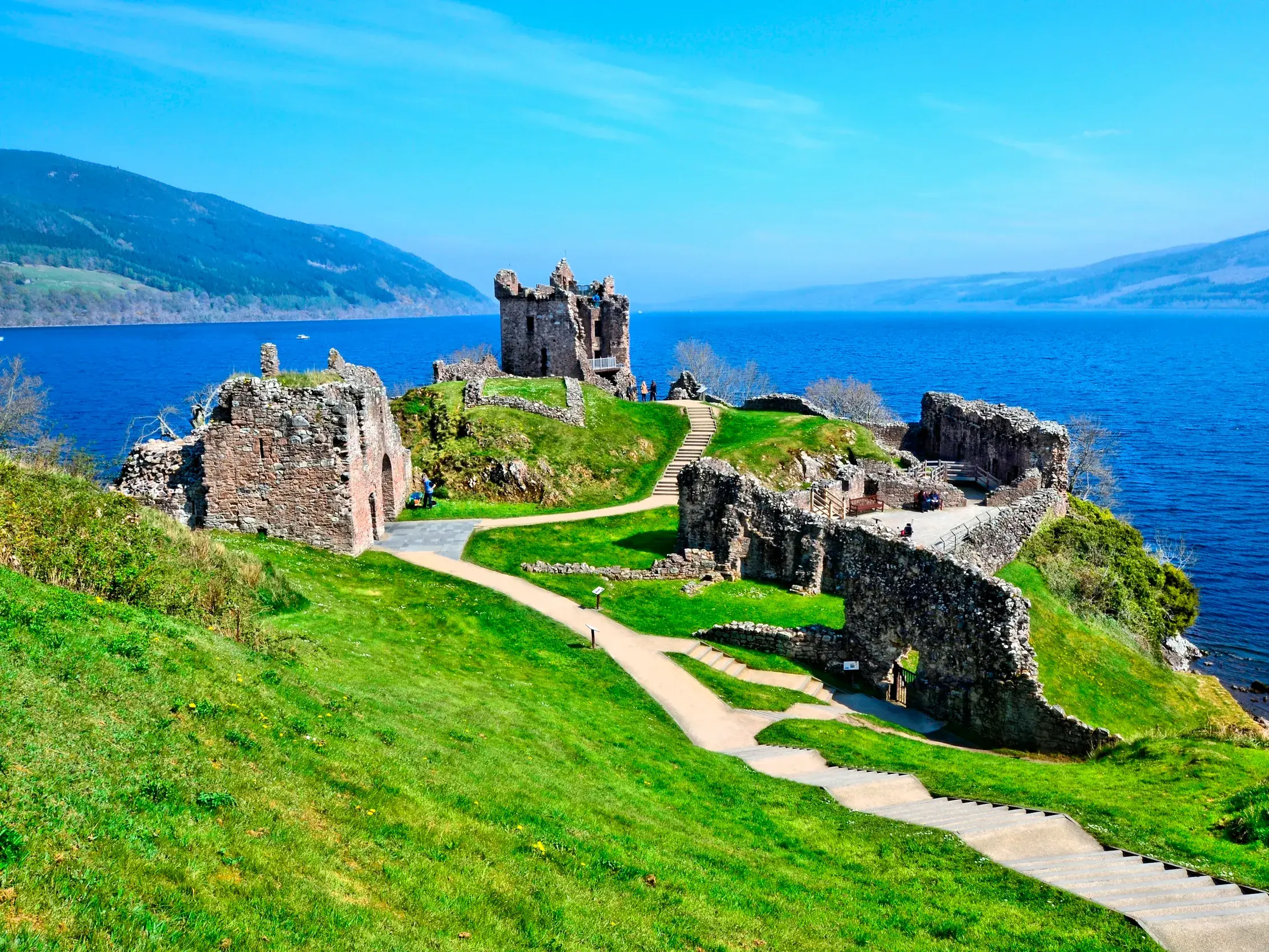 Sonniger Blick auf die historischen Ruinen von Urquhart Castle am Ufer des berühmten Loch Ness in den schottischen Highlands.