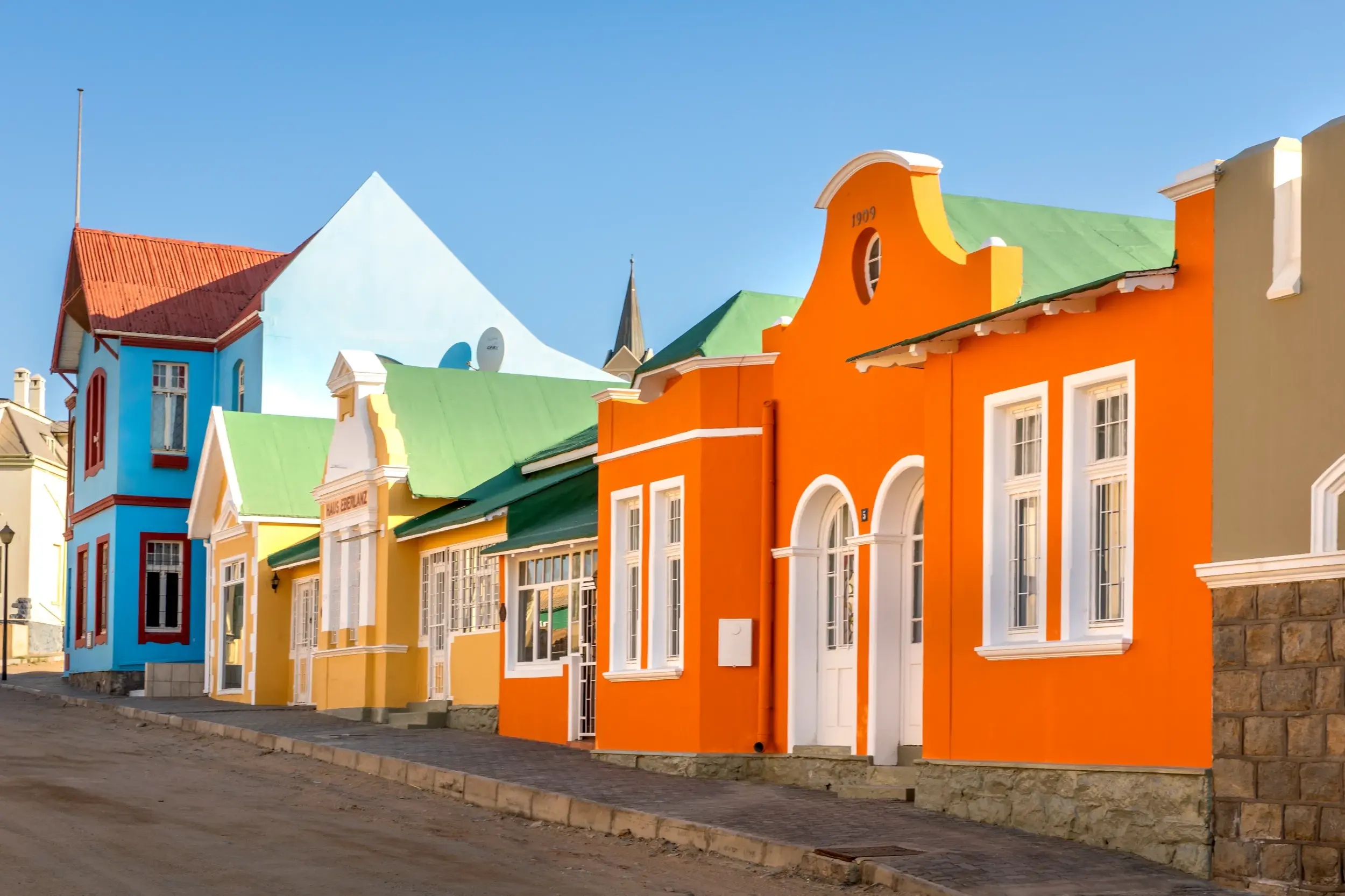 Leuchtend bunte Häuserfassaden im deutschen Kolonialstil säumen eine Straße in der Hafenstadt Lüderitz in Namibia.