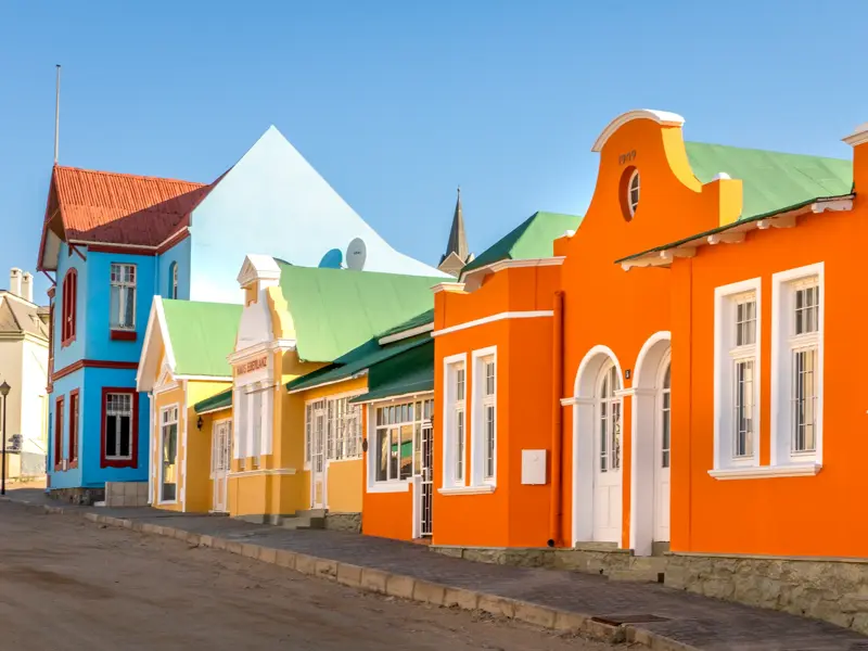 Leuchtend bunte Häuserfassaden im deutschen Kolonialstil säumen eine Straße in der Hafenstadt Lüderitz in Namibia.