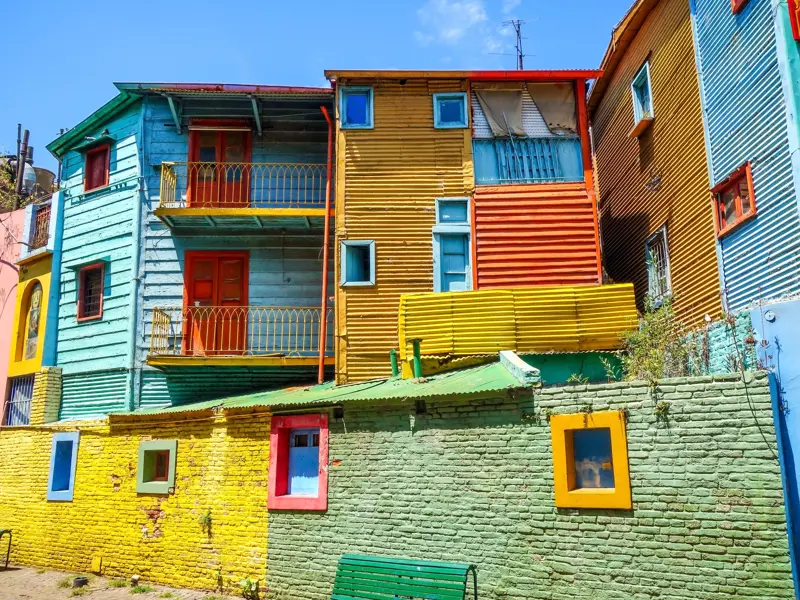 Die berühmten, bunten Wellblechhütten im Hafenviertel La Boca in Buenos Aires unter strahlend blauem Himmel.