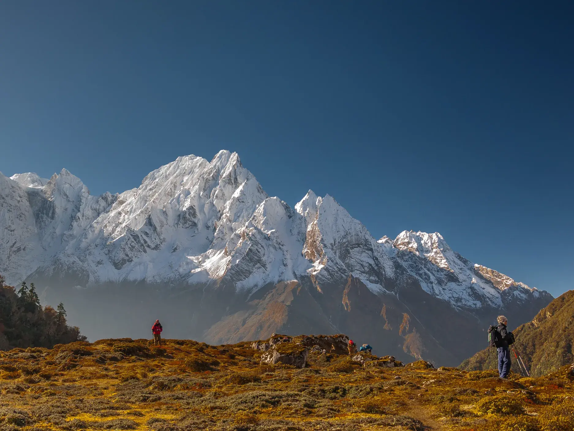 Zwei Wanderer auf einer herbstlichen Hochebene beim Trekking in Nepal mit Panoramablick auf das schneebedeckte Manaslu-Massiv.
