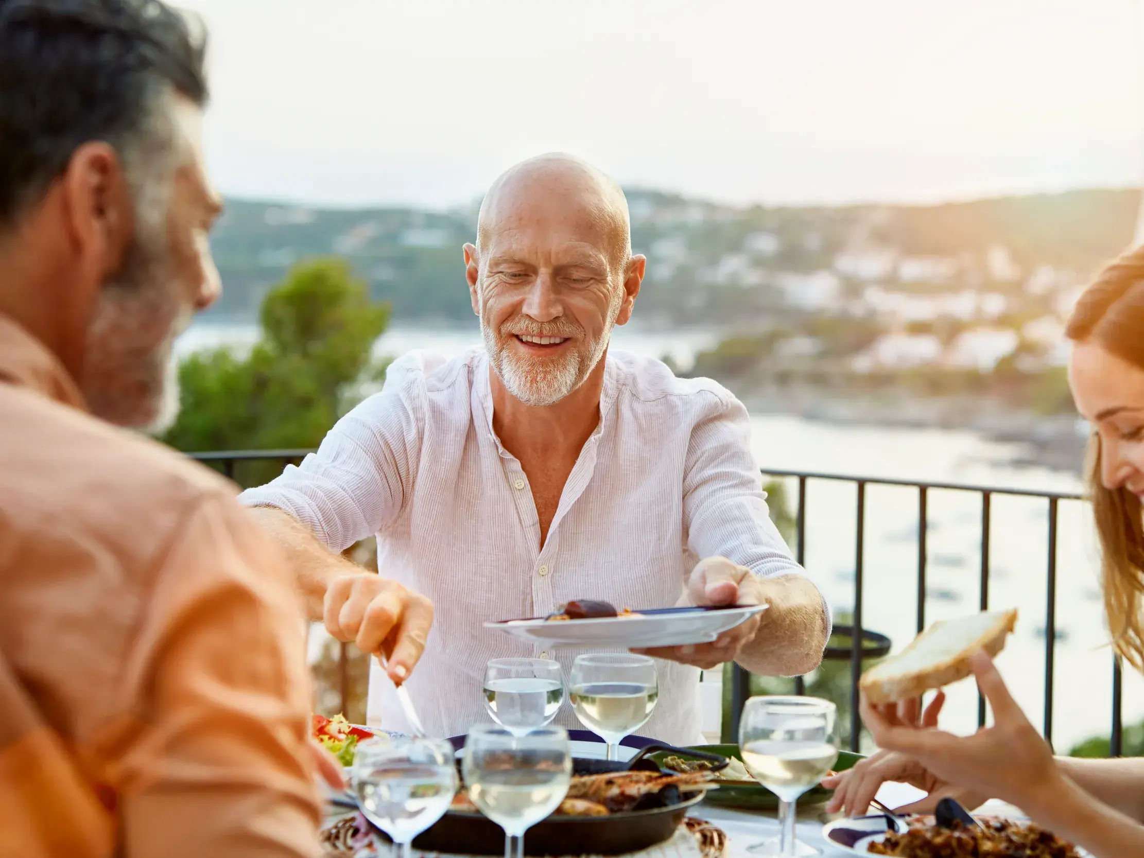 Lächelnde Reisegruppe beim Abendessen mit Wein auf einer Terrasse in Spanien.