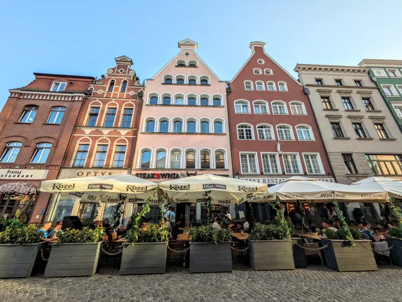 Bunte Giebelhäuser in der Altstadt von Danzig mit einem belebten Straßencafé im Vordergrund bei Sonnenschein.