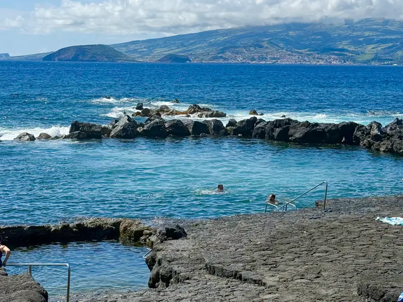 Reisende baden in den Piscinas Naturais auf Sao Miguel, umgeben von schwarzen Lavafelsen und dem tiefblauen Atlantik.
