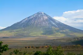 Der heilige Vulkan Ol Doinyo Lengai über der weiten Massai-Steppe in Tansania mit einem traditionellen Boma im Vordergrund.