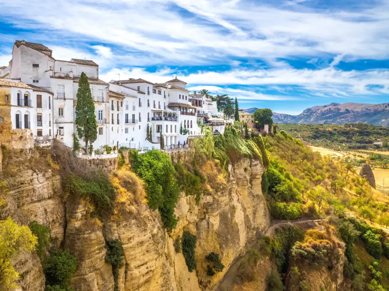 Die weißen Häuser von Ronda thronen an einem sonnigen Tag malerisch über der grünen El Tajo-Schlucht in Andalusien.