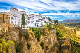 Die weißen Häuser von Ronda thronen an einem sonnigen Tag malerisch über der grünen El Tajo-Schlucht in Andalusien.