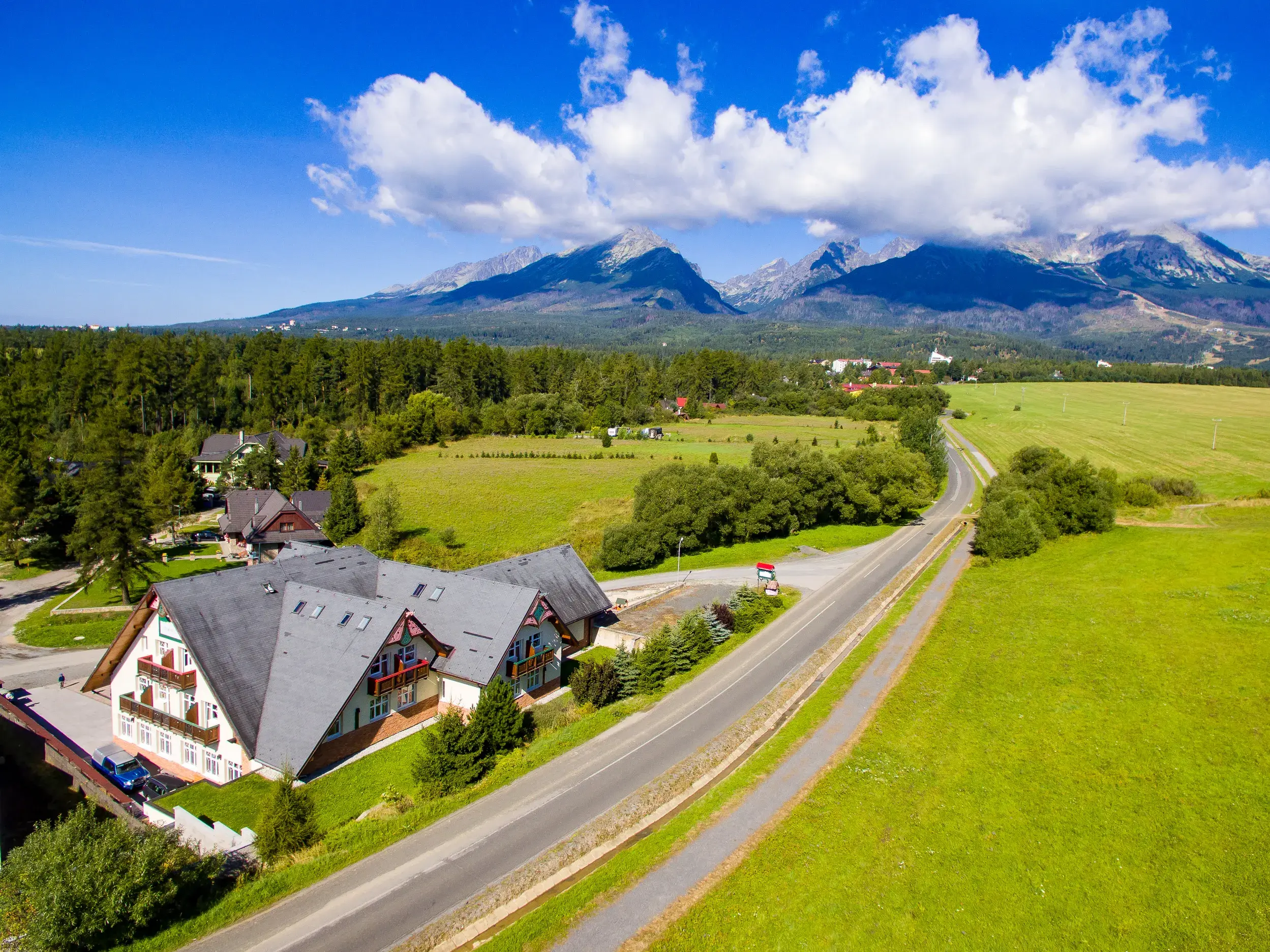 Luftaufnahme der Pension Lomnicky in Stará Lesná, umgeben von Wiesen und Wäldern vor der malerischen Bergkulisse der Hohen Tatra.