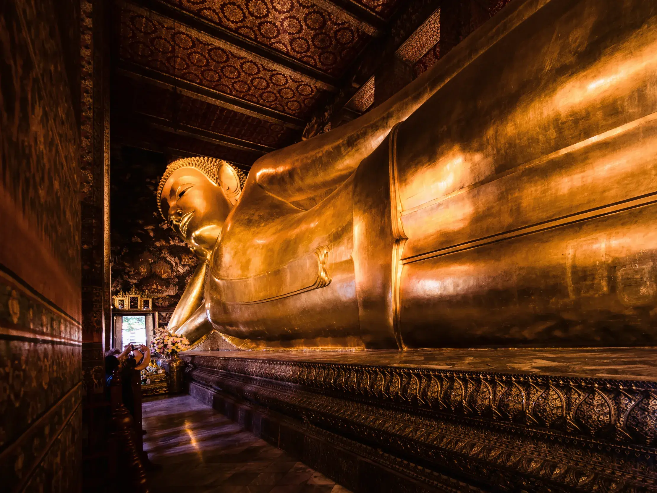 Imposante, goldene Statue des liegenden Buddha im Tempel Wat Pho in Bangkok mit reich verzierter Decke und Sockel.