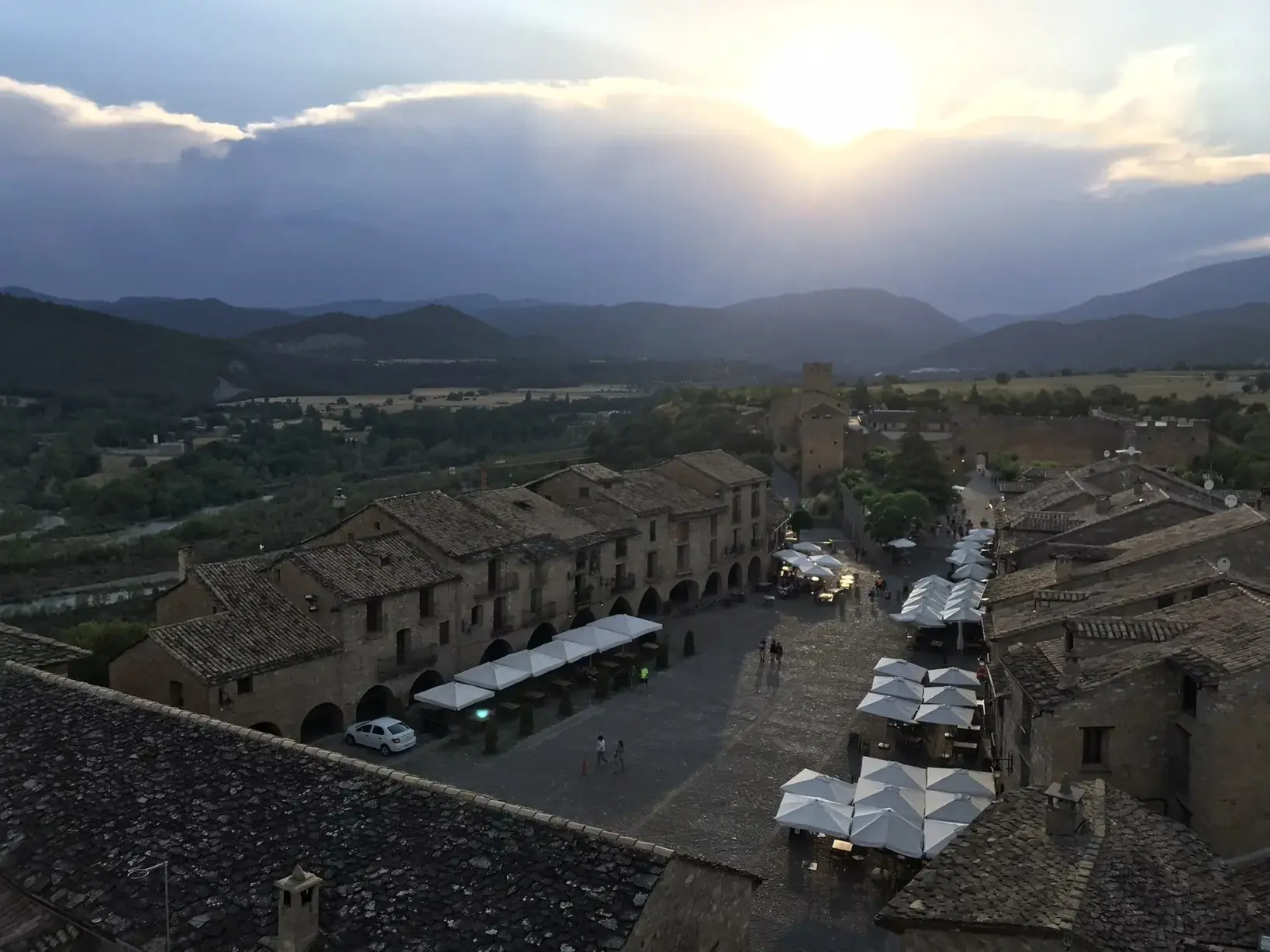 Blick über die Dächer des mittelalterlichen Dorfes Alquézar auf den Dorfplatz bei Sonnenuntergang mit Bergkulisse der Pyrenäen.