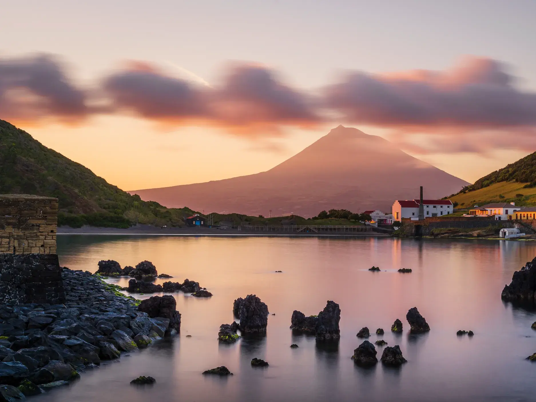 Majestätischer Vulkan Pico auf der Azoren-Insel Pico bei Sonnenuntergang, gesehen über eine ruhige Bucht mit Vulkanfelsen.