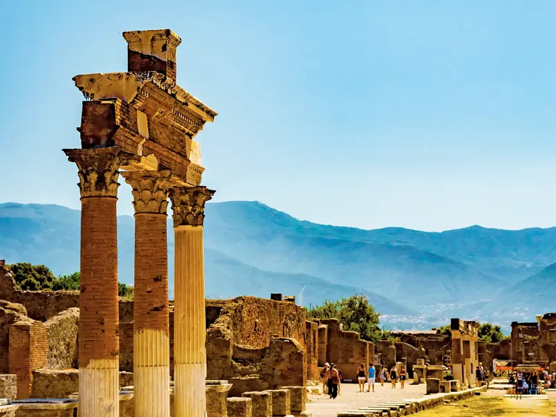 Korinthische Säulen in der Ausgrabungsstätte von Pompeji bei einer Studiosus Studienreise mit Blick auf die Berge am Golf von Neapel.