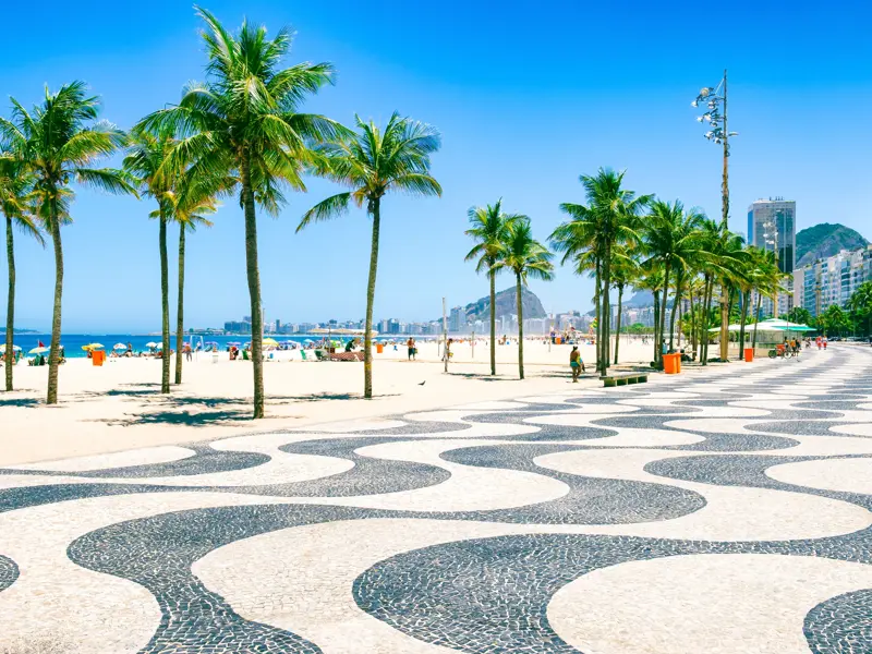 Berühmte Mosaik-Promenade an der Copacabana in Rio de Janeiro mit Palmen und Sandstrand.