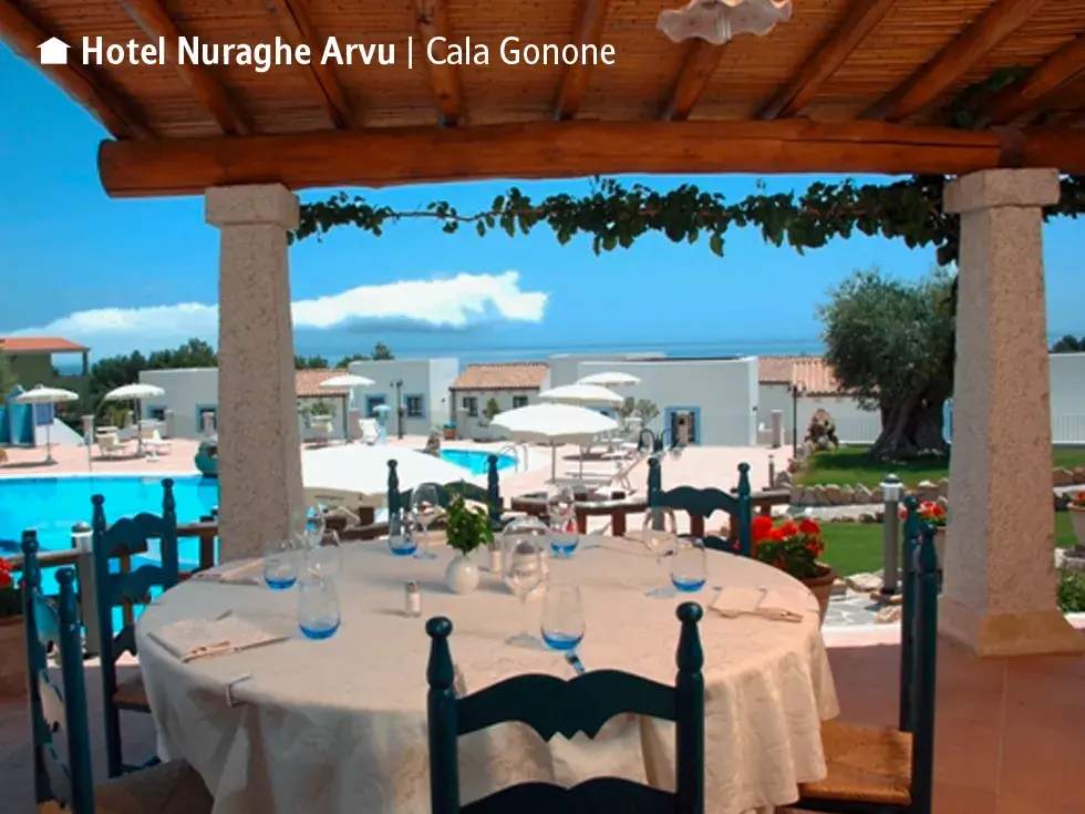 Gedeckter Tisch auf der Terrasse des Hotels Nuraghe Arvu mit Blick auf den Pool, die Hotelanlage und das Meer in Cala Gonone.