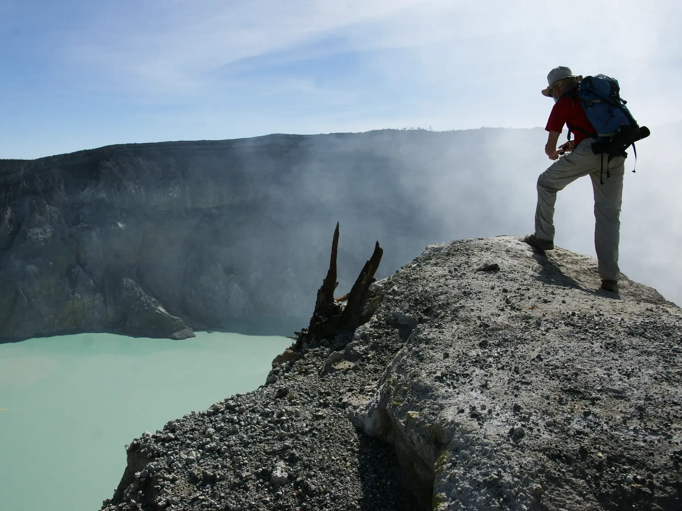 Ein Wanderer steht am Kraterrand des Gunung Ijen und blickt auf den leuchtend türkisfarbenen, dampfenden Kratersee auf Java.