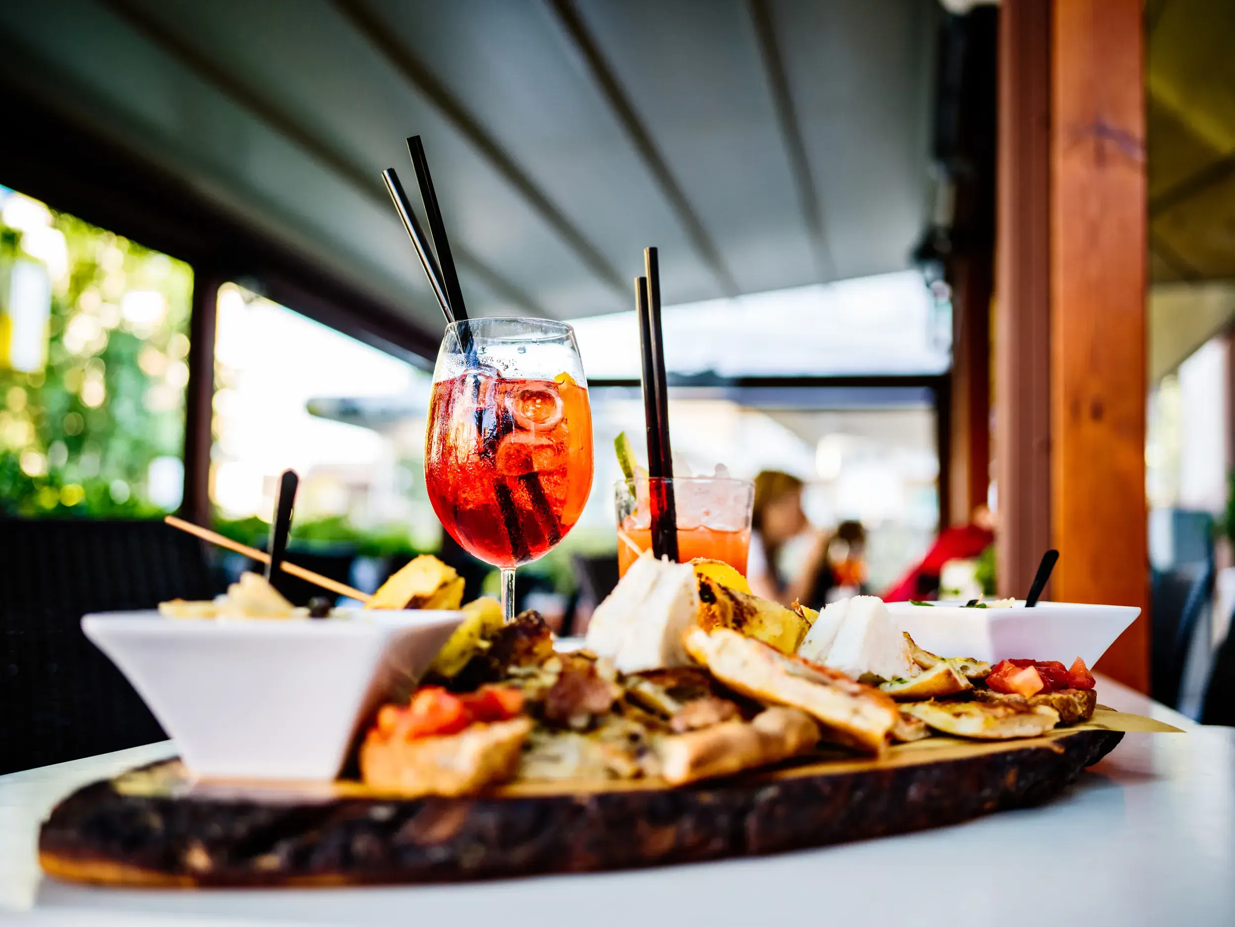 Ein Aperitif und eine Holzplatte mit sizilianischen Antipasti auf dem Tisch auf der Terrasse einer Trattoria.
