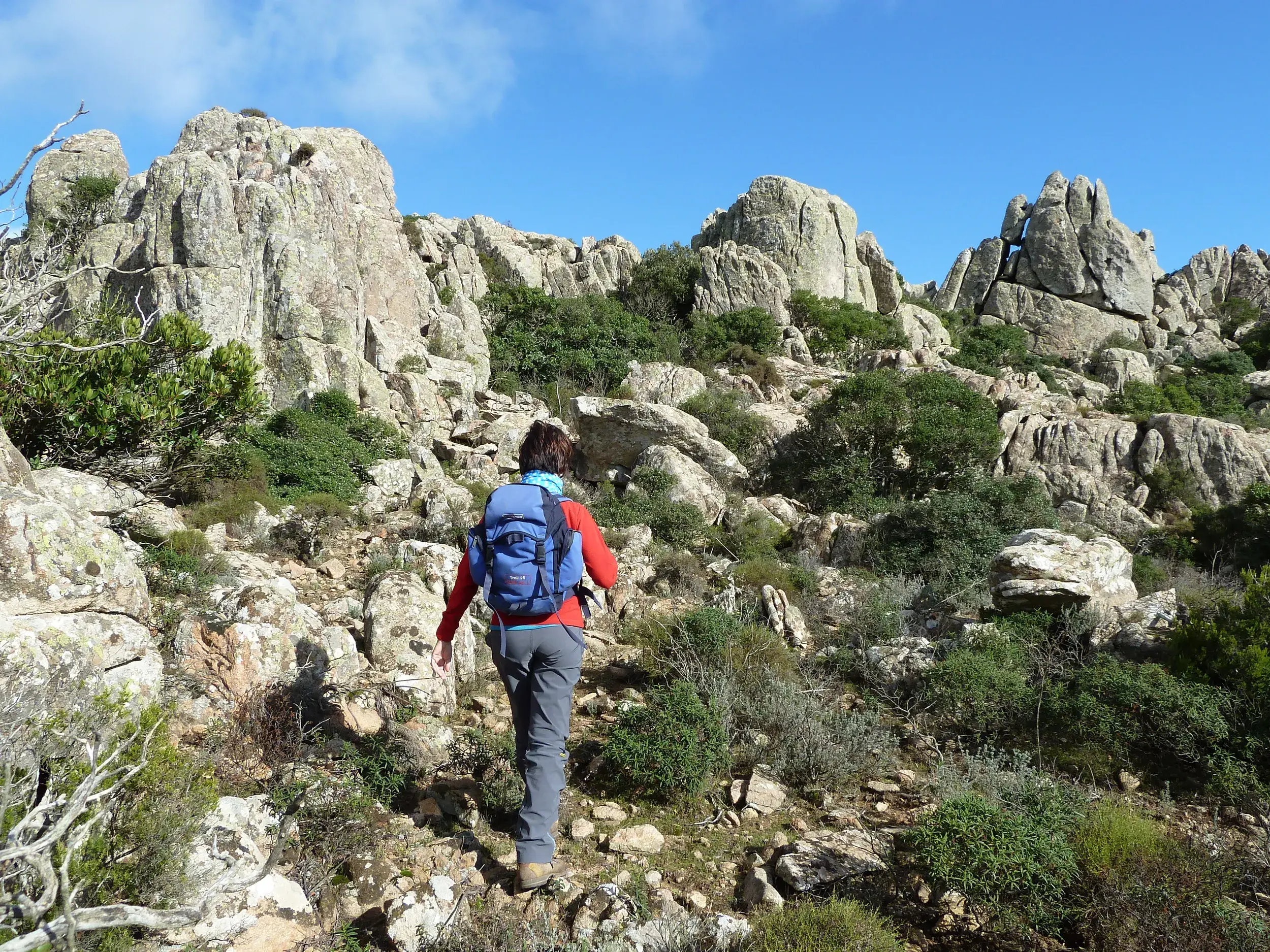 Eine Frau mit Rucksack wandert auf einem steinigen Pfad durch die bizarre Granitlandschaft des I Sette Fratelli auf Sardinien.