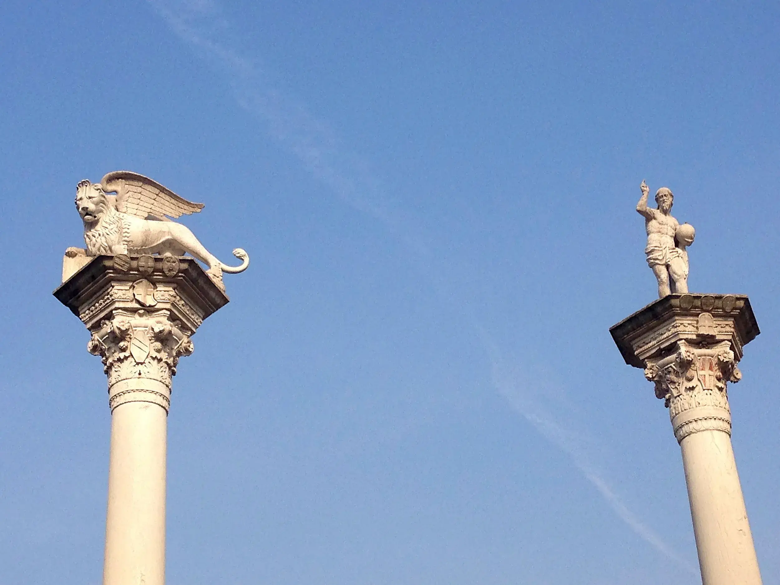 Die Säulen des Markus mit dem geflügelten Löwen und des Theodors am Eingang zum Markusplatz in Venedig vor blauem Himmel.