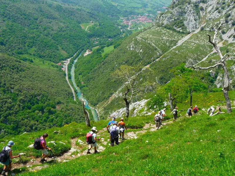Eine Wandergruppe steigt auf einem schmalen Bergpfad ab, mit weitem Blick über ein grünes Tal in den Picos de Europa, Spanien.