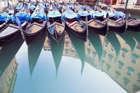 Ikonische schwarze Gondeln liegen in einem ruhigen Seitenkanal Venedigs, ihre Silhouetten spiegeln sich im Wasser.