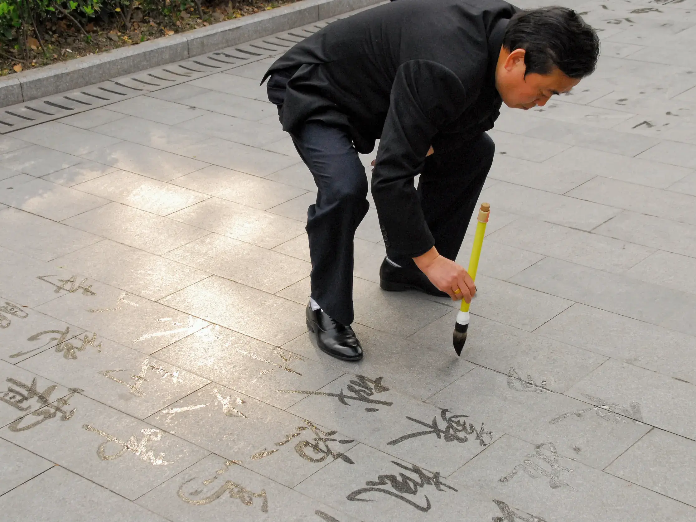 Einheimischer Künstler malt in China mit einem großen Pinsel und Wasser vergängliche Kalligrafie-Zeichen auf den Gehweg.