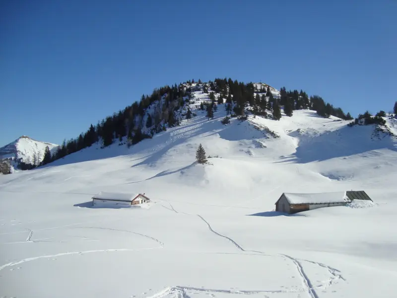 Schneeschuhspuren führen zu zwei Almhütten in der unberührten Winterlandschaft des Risstals im Karwendel.