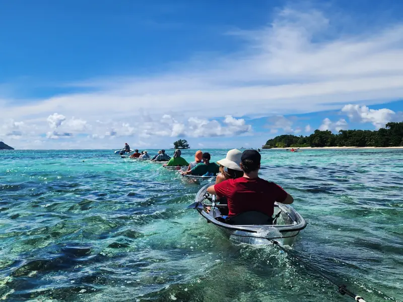 Reisegruppe auf Kajaktour mit transparenten Booten im türkisen Meer vor dem berühmten Strand Source d'Argent auf La Digue.