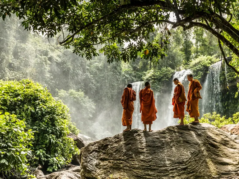 Vier buddhistische Mönche in orangen Roben stehen auf einem Felsen und betrachten den Phnom Kulen Wasserfall in Kambodscha.