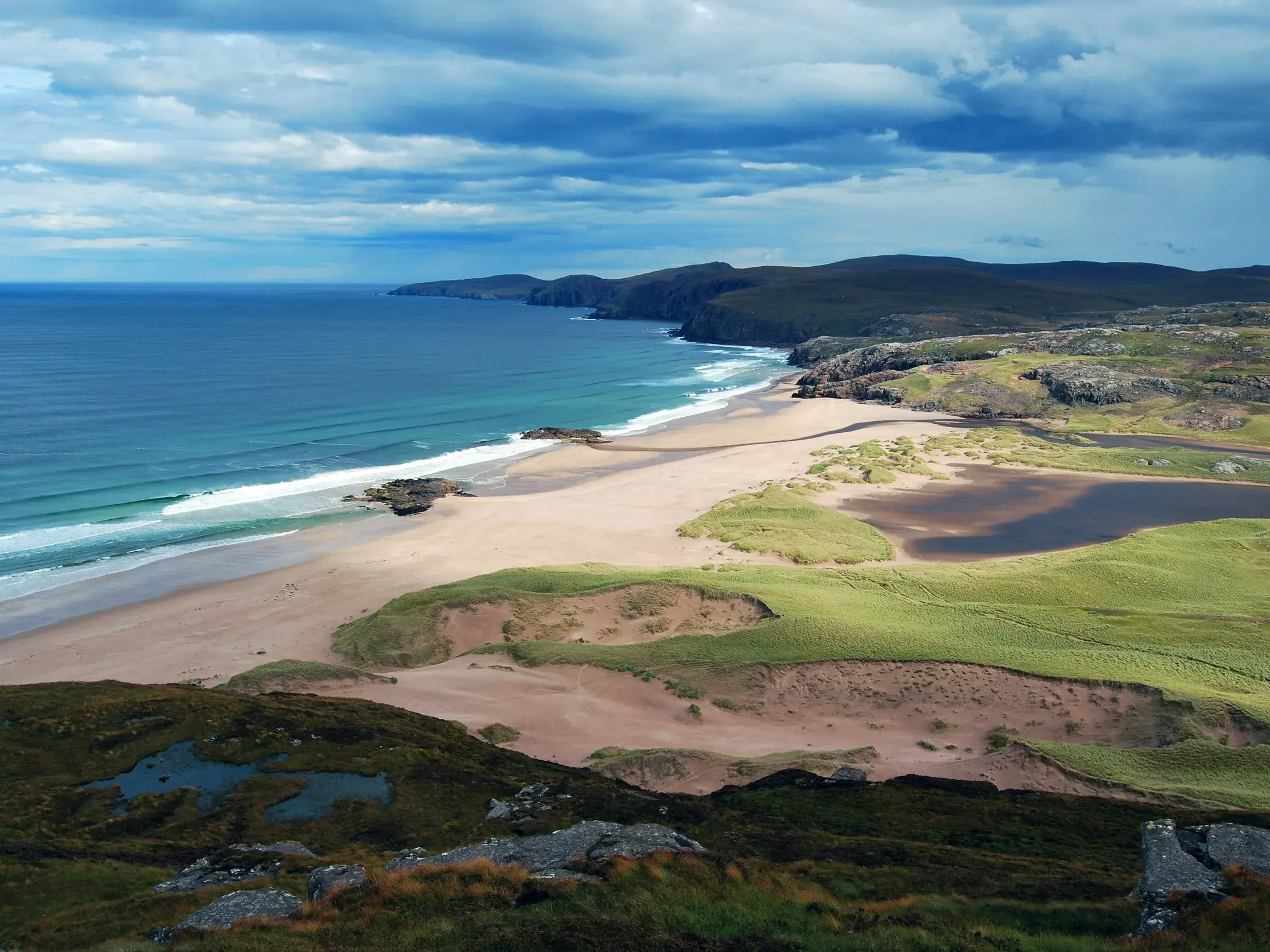 Blick von einer Küstenwanderung auf die abgelegene Sandwood Bay mit Dünenlandschaft und dem Atlantik in Schottland.