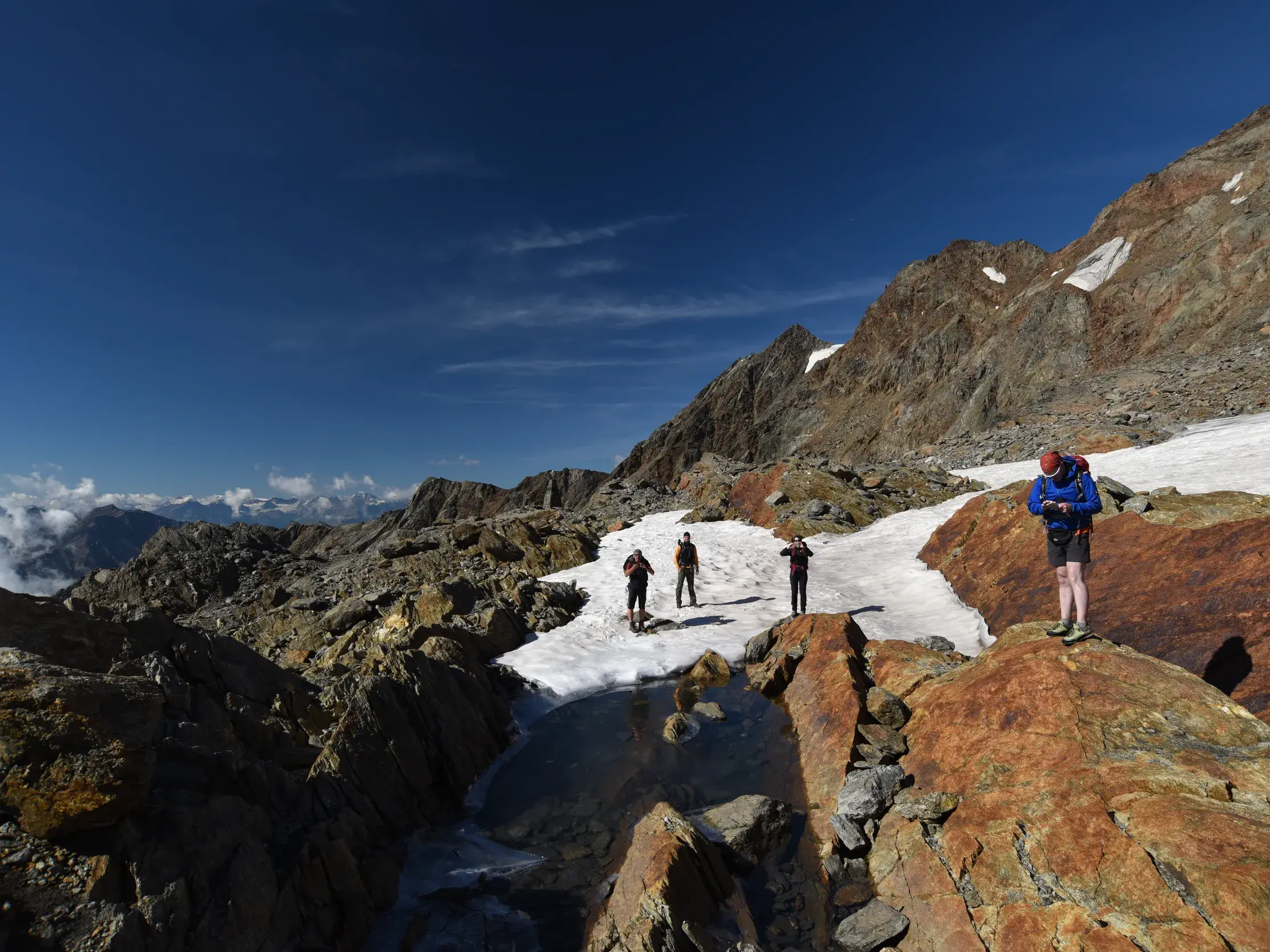 Vier Wanderer auf einem Schneefeld in der felsigen Hochgebirgslandschaft der Ötztaler Alpen nahe des Pitztaler Jöchls.