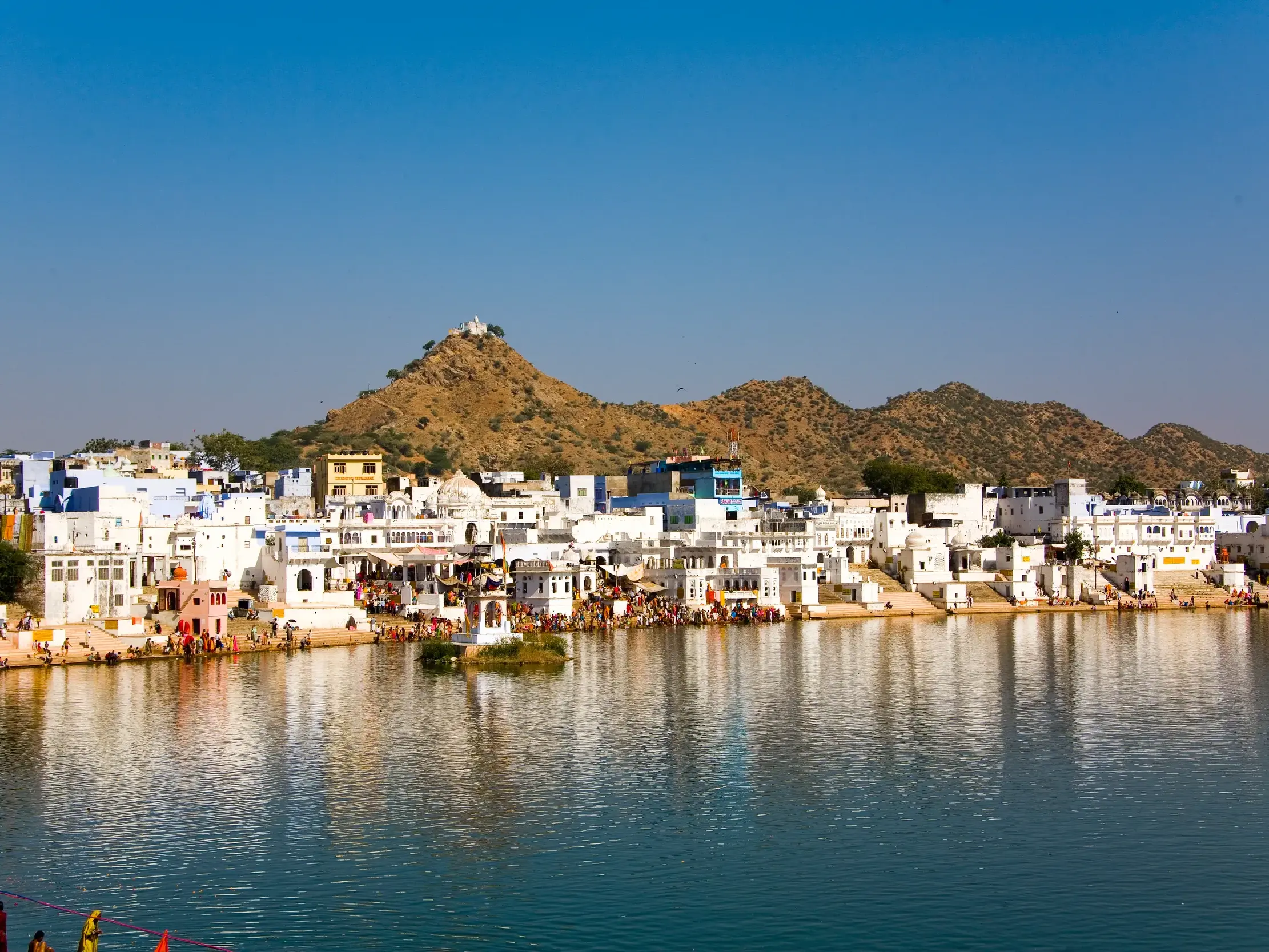 Blick auf die heilige Stadt Pushkar mit ihren weißen Gebäuden am Ufer des Pushkar-Sees und dem Savitri-Tempel im Hintergrund.