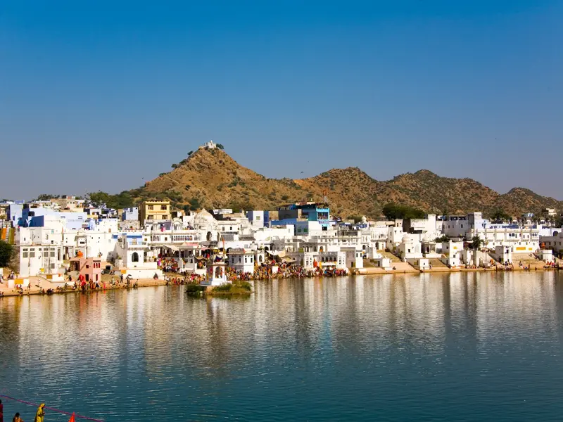 Blick auf die heilige Stadt Pushkar mit ihren weißen Gebäuden am Ufer des Pushkar-Sees und dem Savitri-Tempel im Hintergrund.