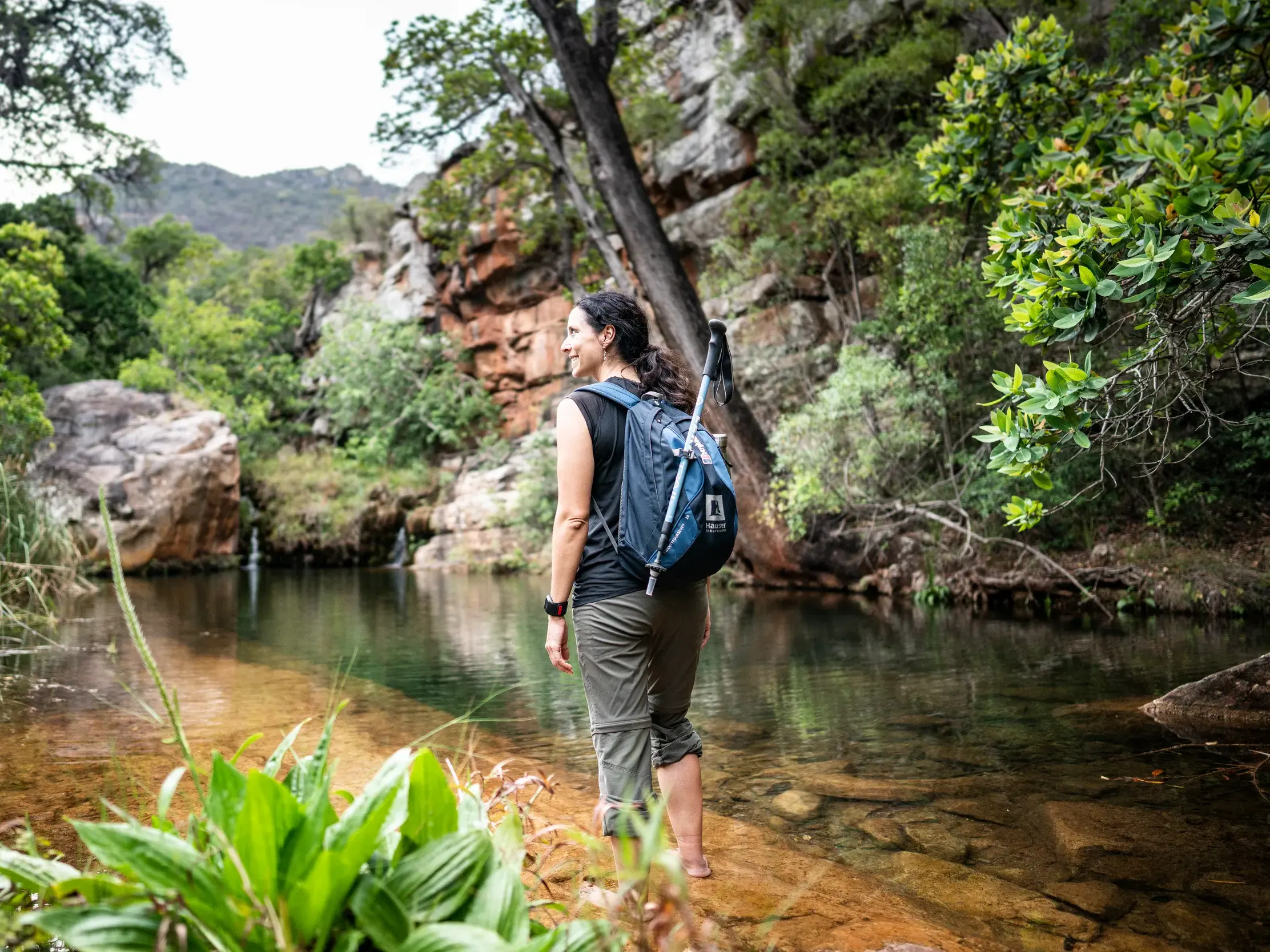Wanderin mit Trekkingrucksack bei einer Barfuß-Pause an einem Fluss in den südafrikanischen Drakensbergen.