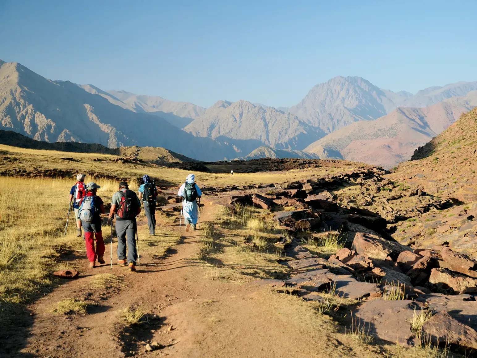 Eine Hauser-Reisegruppe mit lokalem Guide beim Slow-Trekking durch die weite Berglandschaft des Hohen Atlas in Marokko.