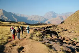 Eine Hauser-Reisegruppe mit lokalem Guide beim Slow-Trekking durch die weite Berglandschaft des Hohen Atlas in Marokko.