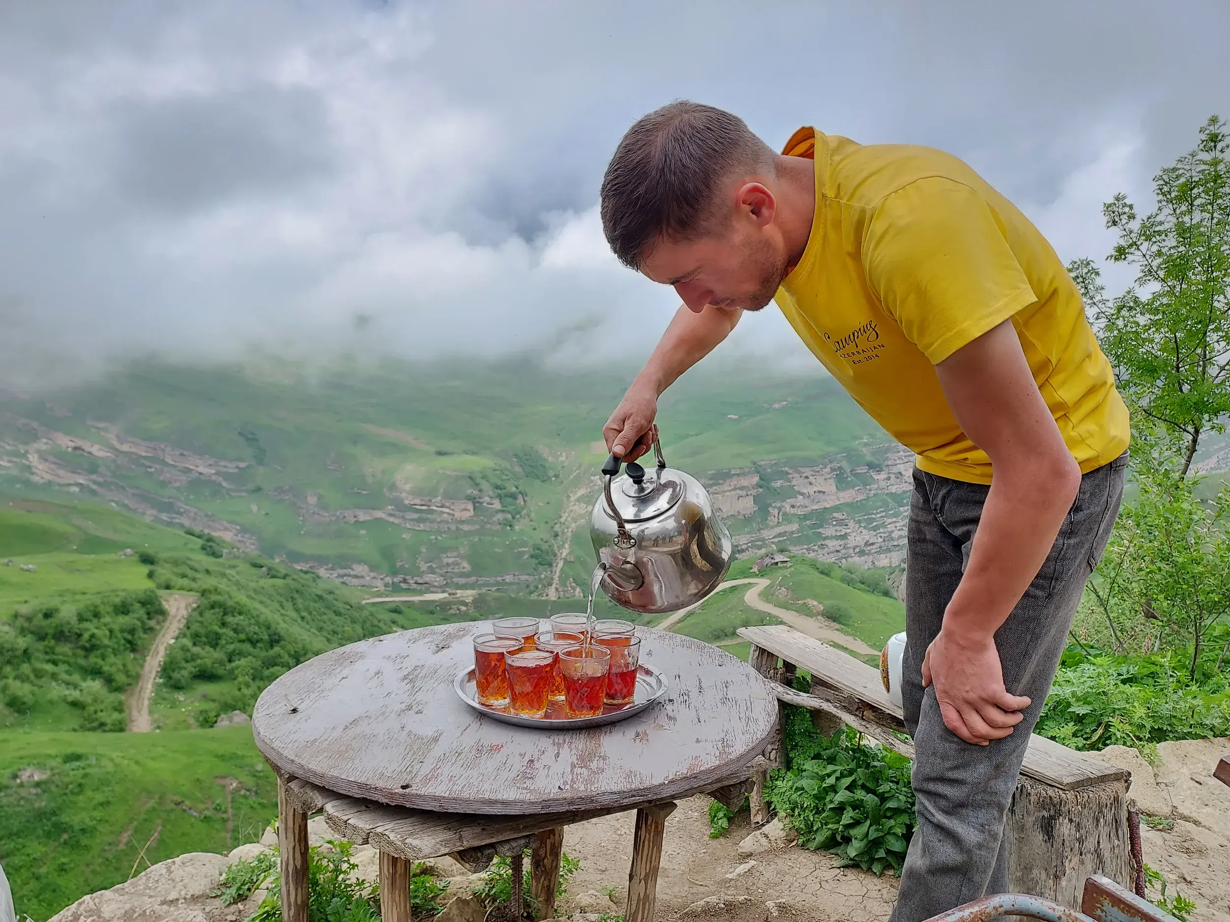 Teepause während einer Trekkingtour: Ein Mann schenkt Tee ein vor der grünen Berglandschaft des Großen Kaukasus.